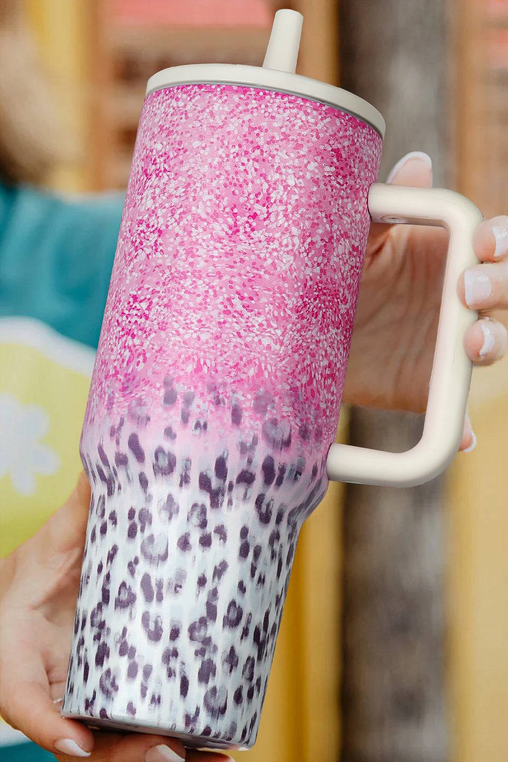 Pink and white speckled tumbler with a leopard print base held by a hand.