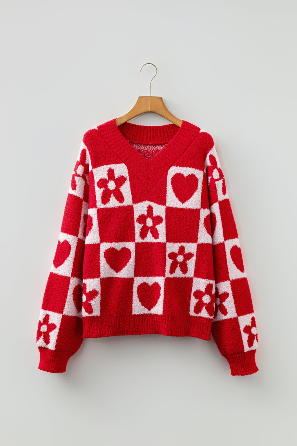 Red and white checkered sweater with heart and flower patterns on a hanger against a light gray background