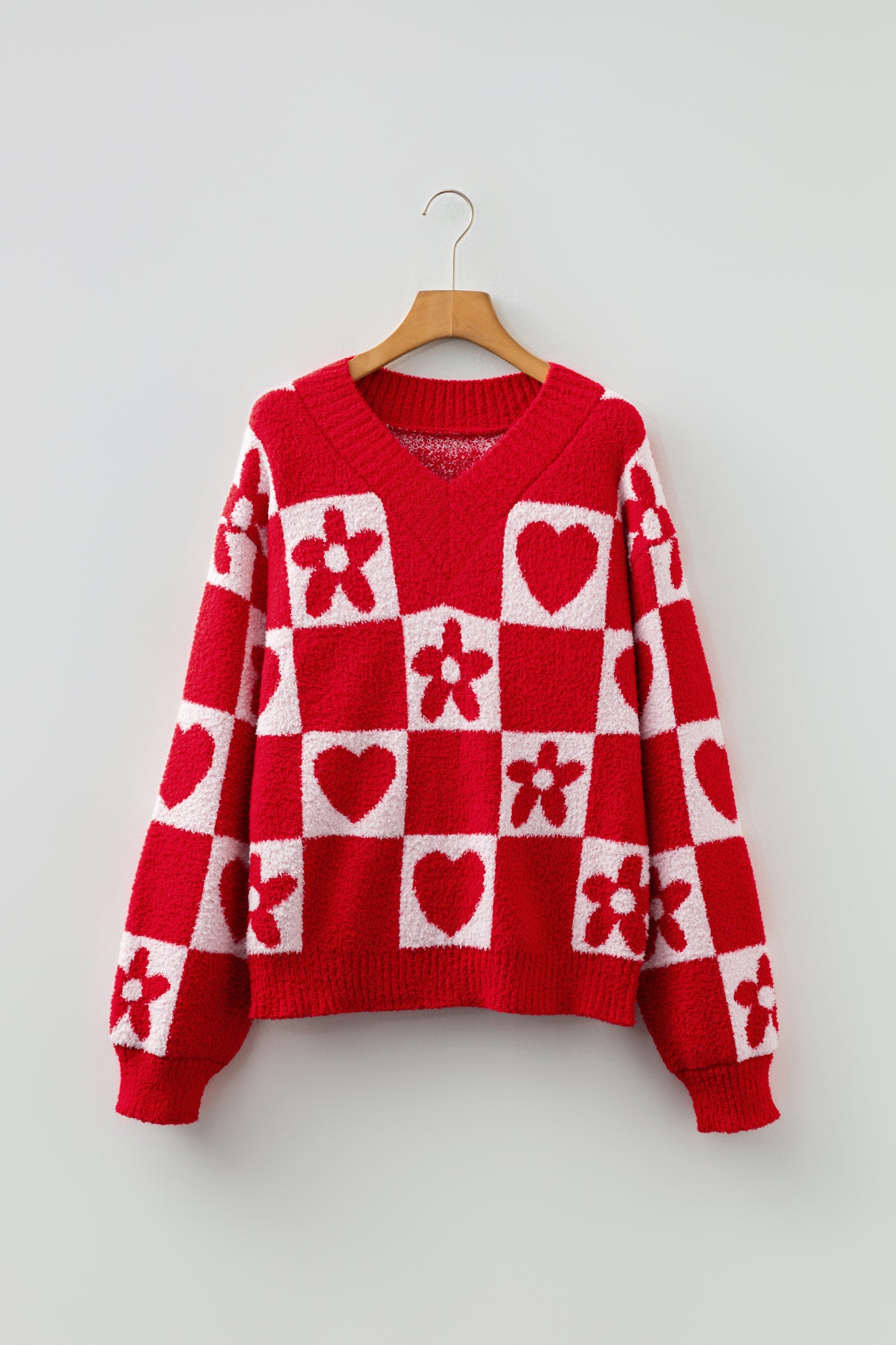 Red and white checkered sweater with heart and flower patterns on a hanger against a light gray background