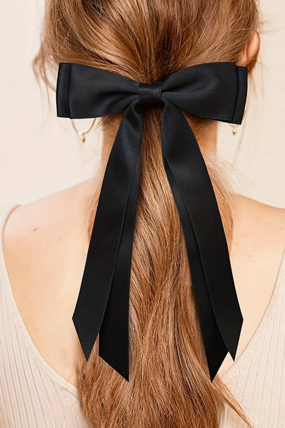 Black hair bow tied in a ponytail with a neutral background
