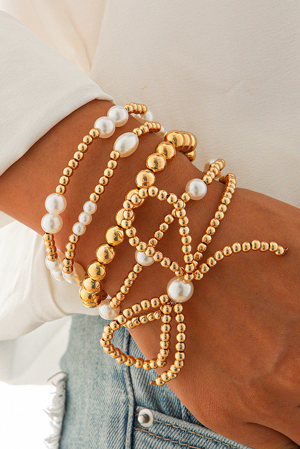 Gold and pearl beaded bracelets on a wrist with a blurred background