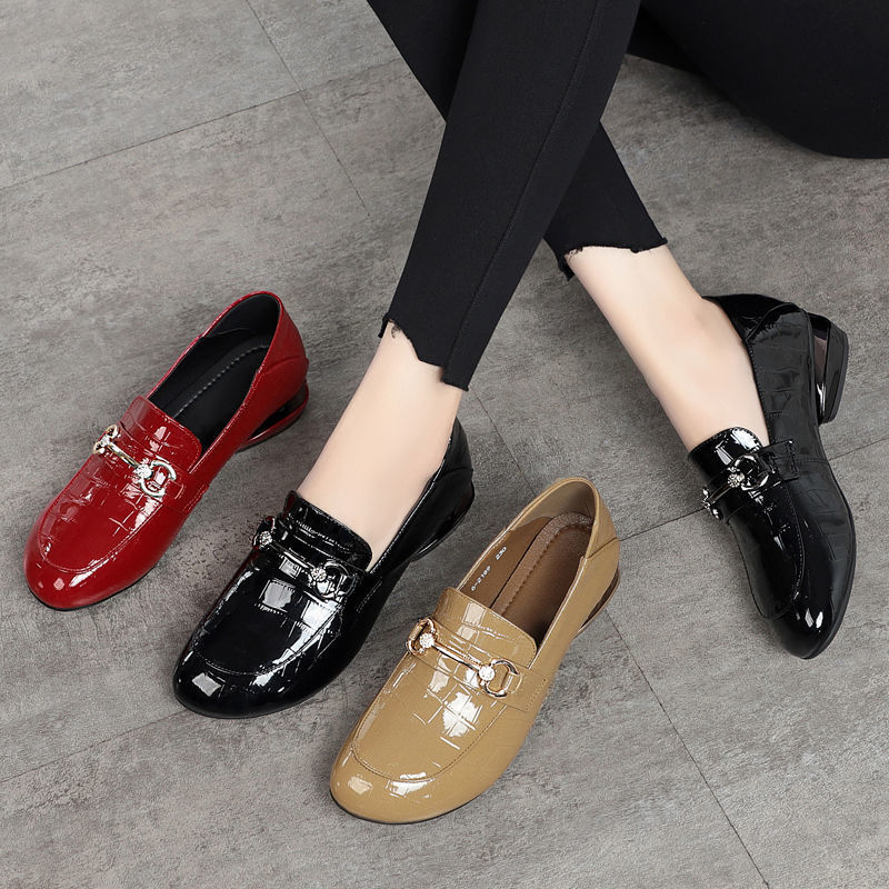 Four shiny loafers in red, black, and beige on a gray floor.