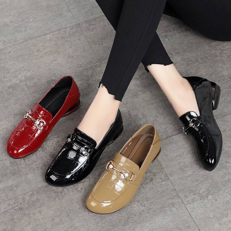 Four shiny loafers in red, black, and beige on a gray floor.