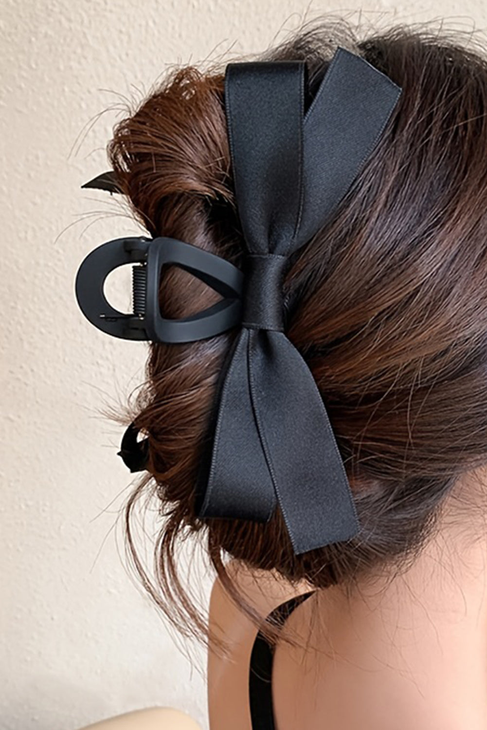 Black hair bow accessory on a person's hair against a neutral background