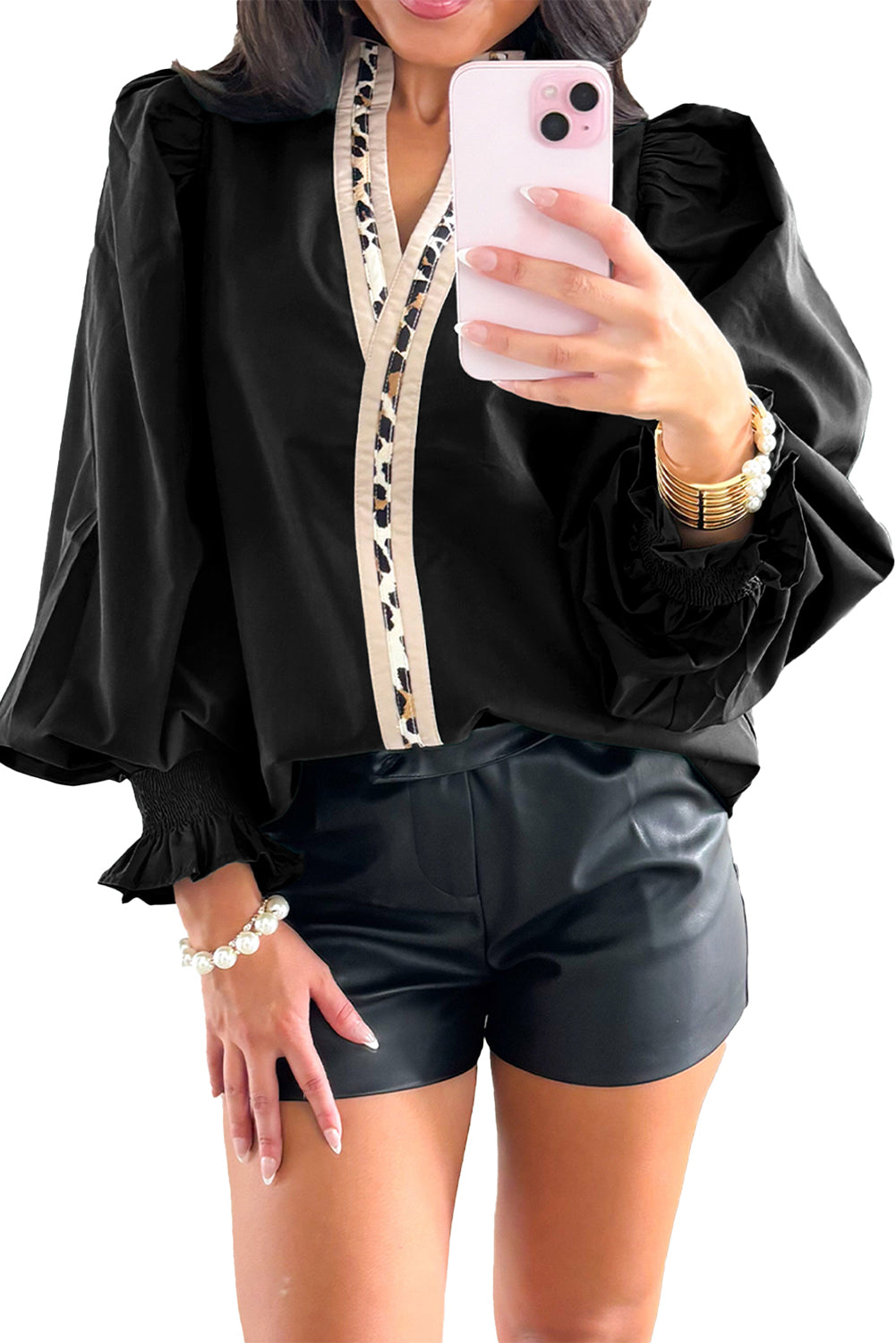 Person wearing a black outfit with ruffled sleeves and a white zipper, holding a pink phone.