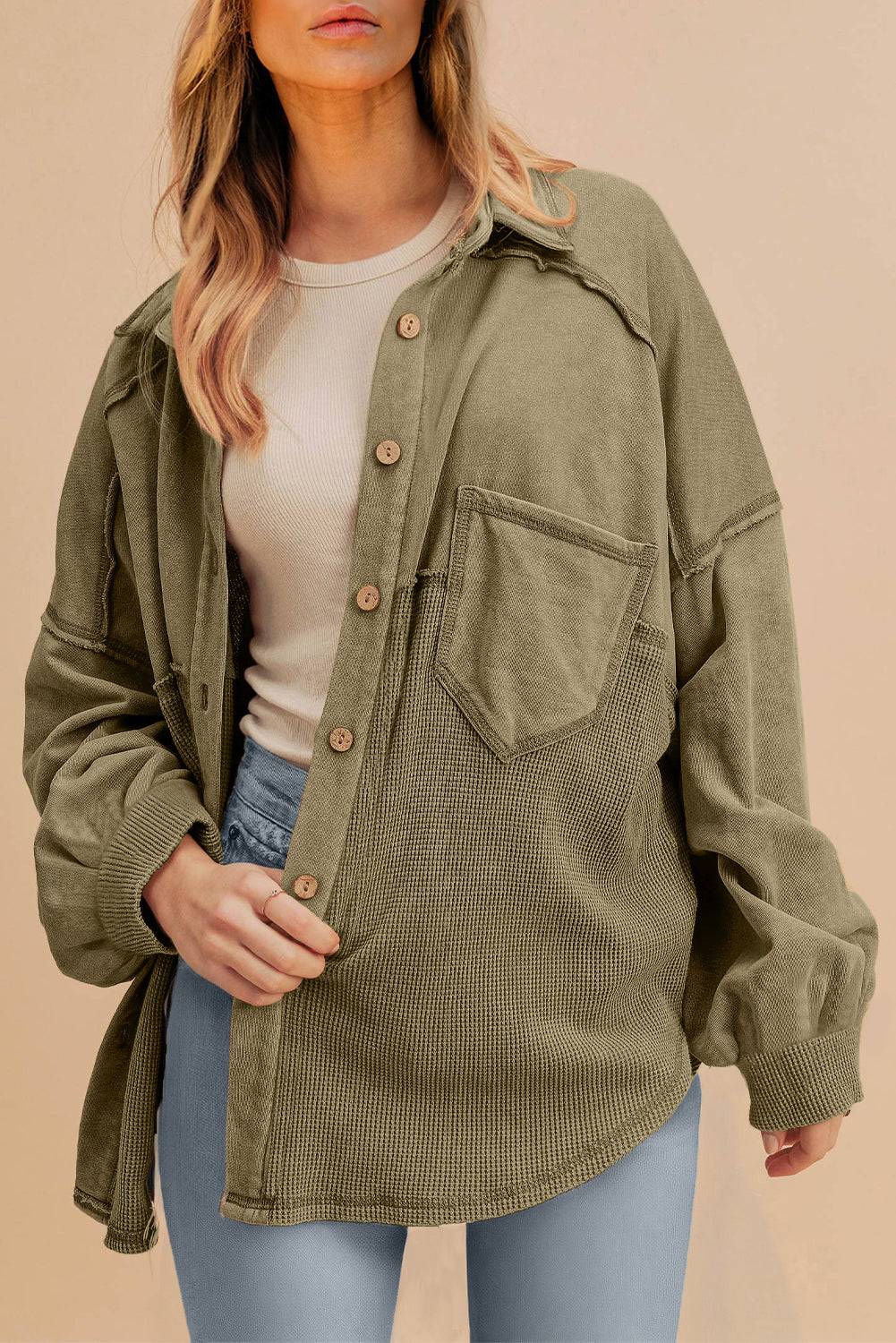 Person wearing an olive green jacket over a white shirt and blue jeans on a beige background