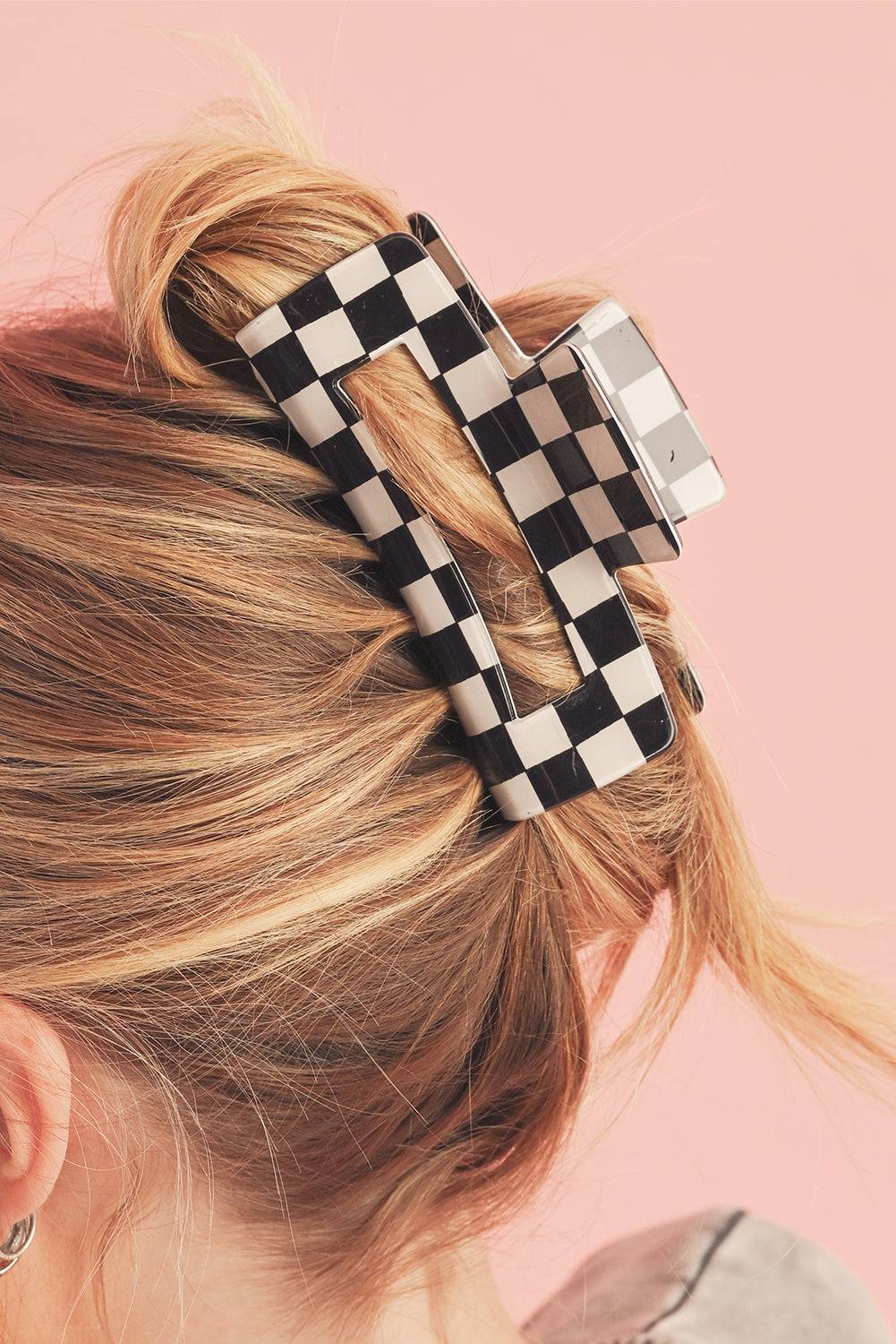 Checkered hair clip in blonde hair against a pink background