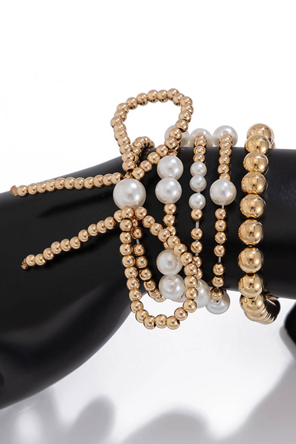 Gold and pearl beaded bracelets on a black hand model against a white background