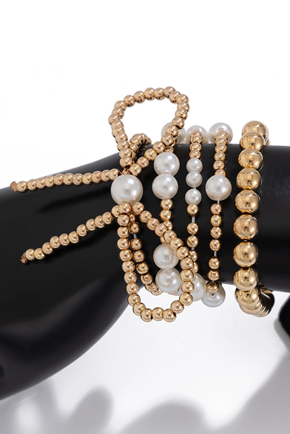 Gold and pearl beaded bracelets on a black hand model against a white background