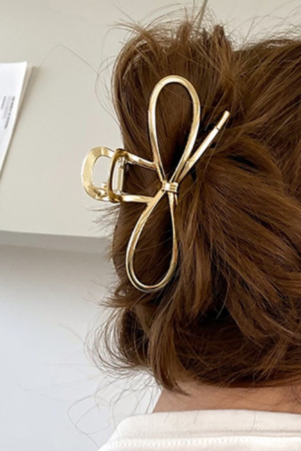 Gold bow hair clip in a person's hair with a neutral background