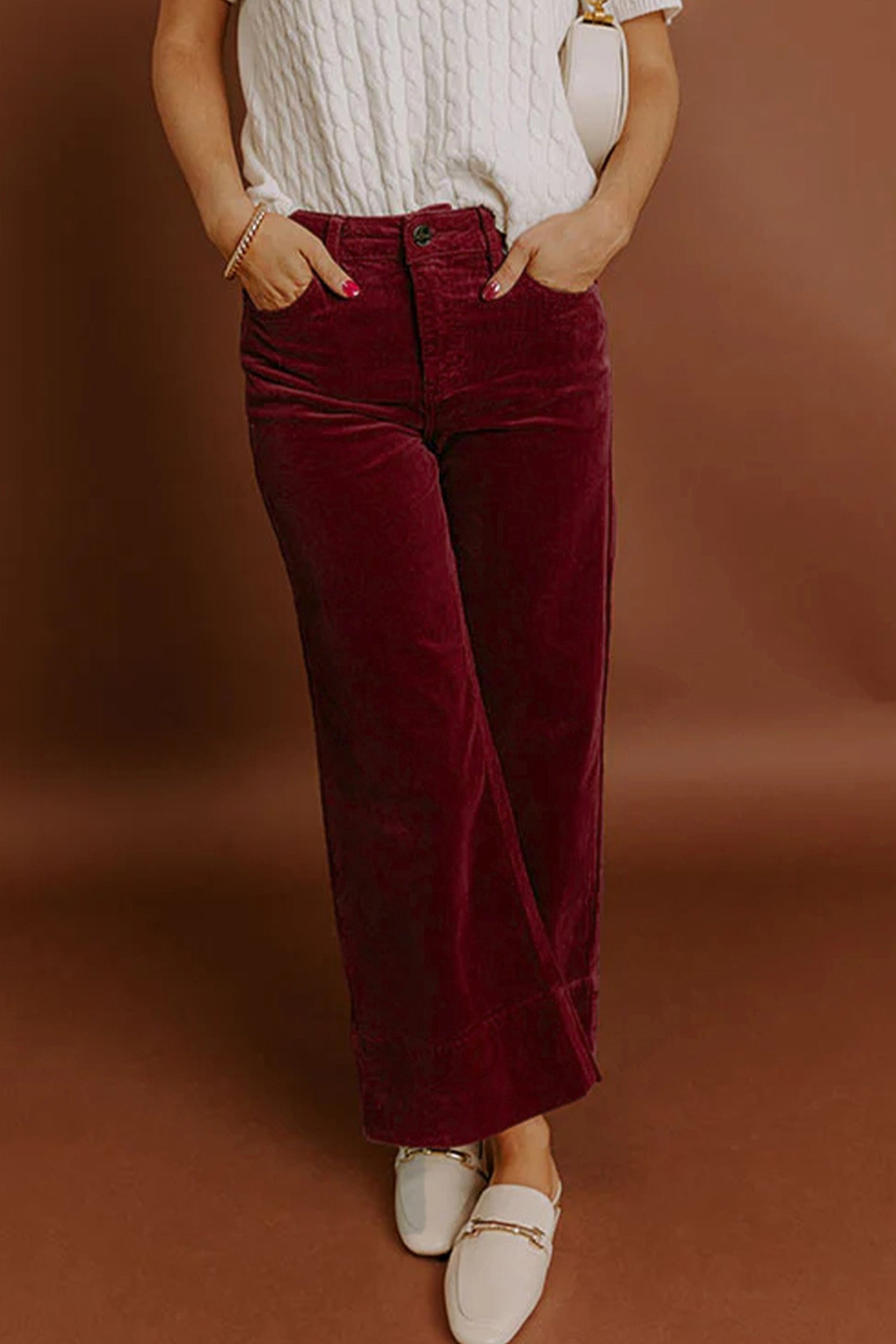 Person wearing burgundy velvet pants with a white top against a brown background