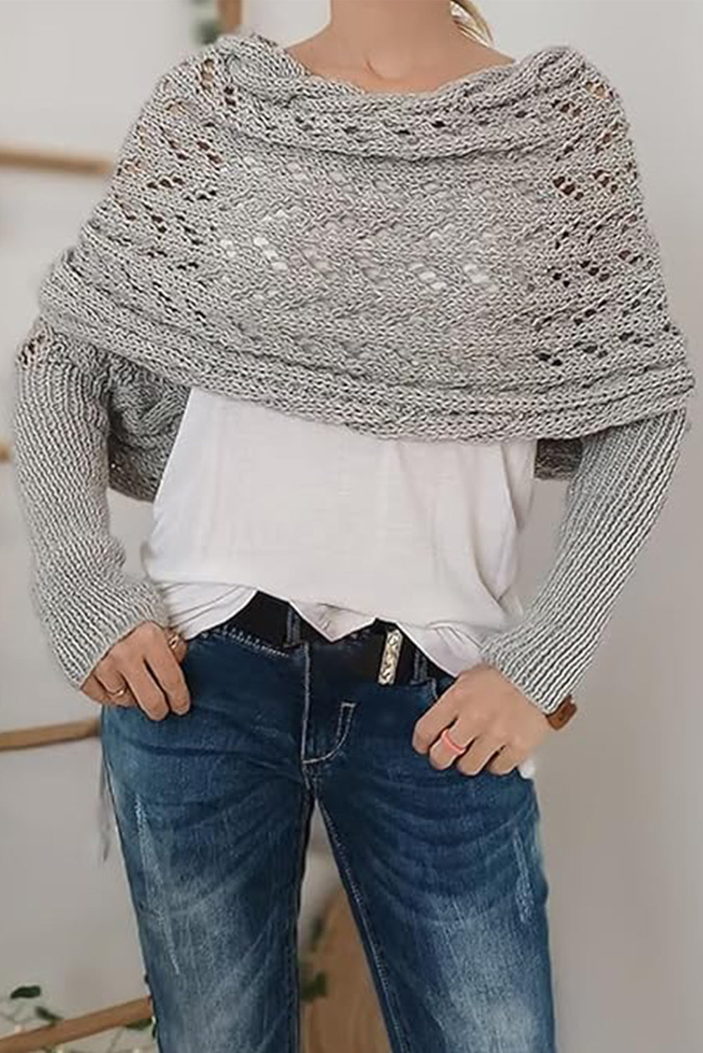 Person wearing a gray knitted shawl over a white shirt and blue jeans.
