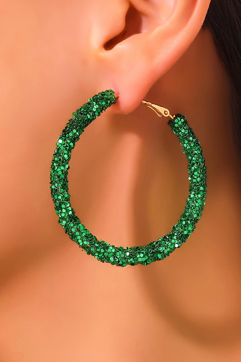 Green hoop earring worn on a model's ear against a neutral background
