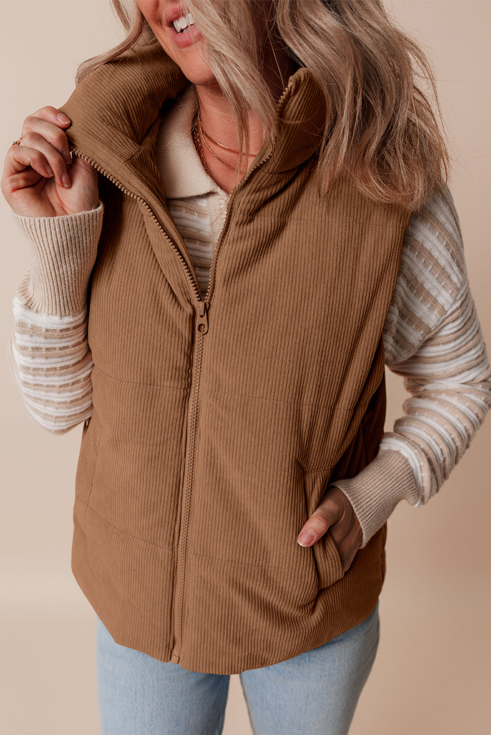 Woman wearing a brown corduroy vest over a striped shirt with a beige background