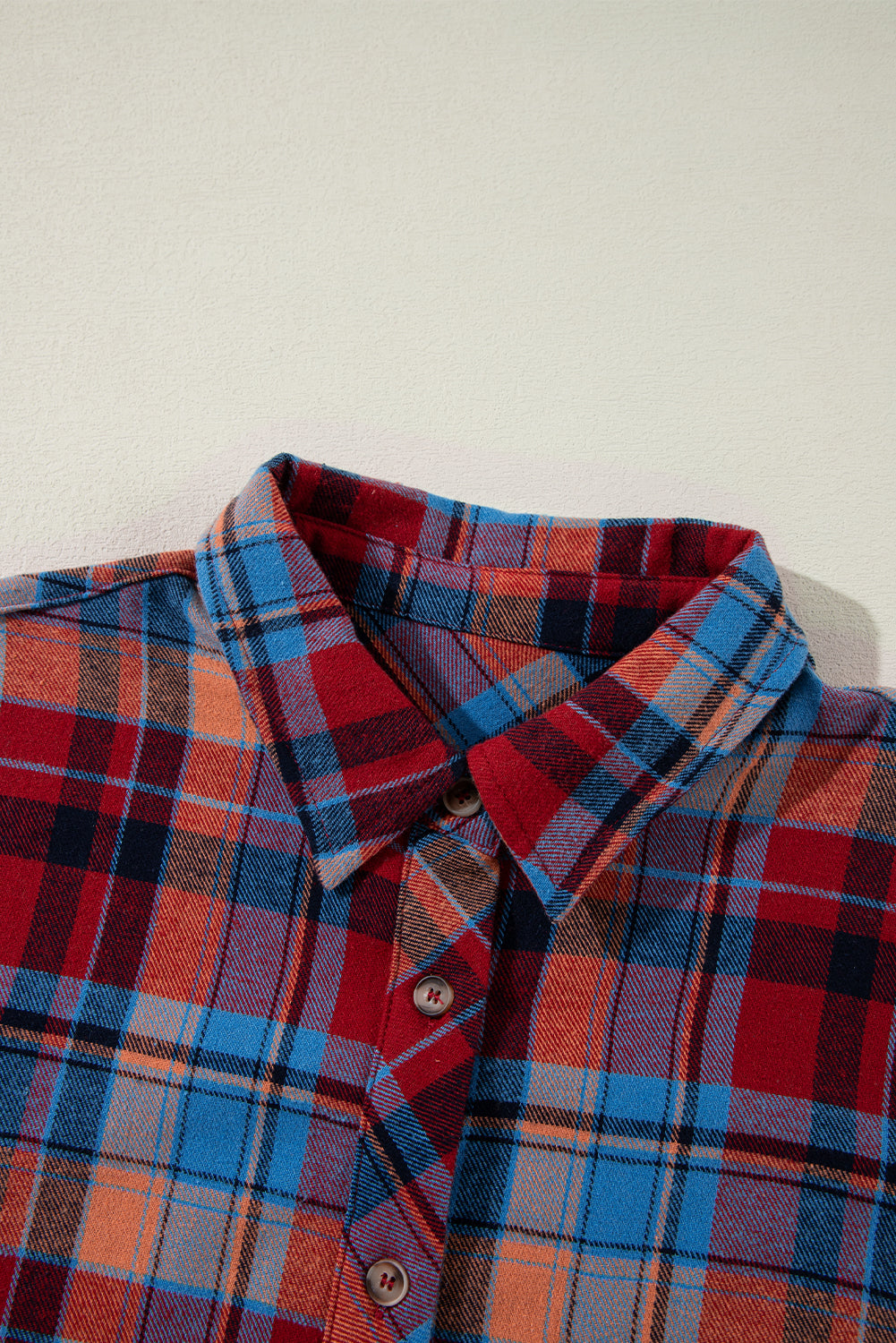 Close-up of a plaid shirt with red, blue, and orange colors on a white background
