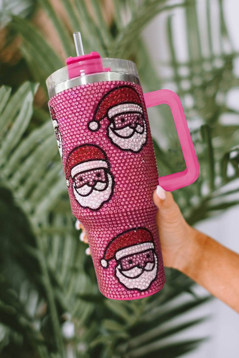 Pink tumbler with Santa face design held against a green leafy background