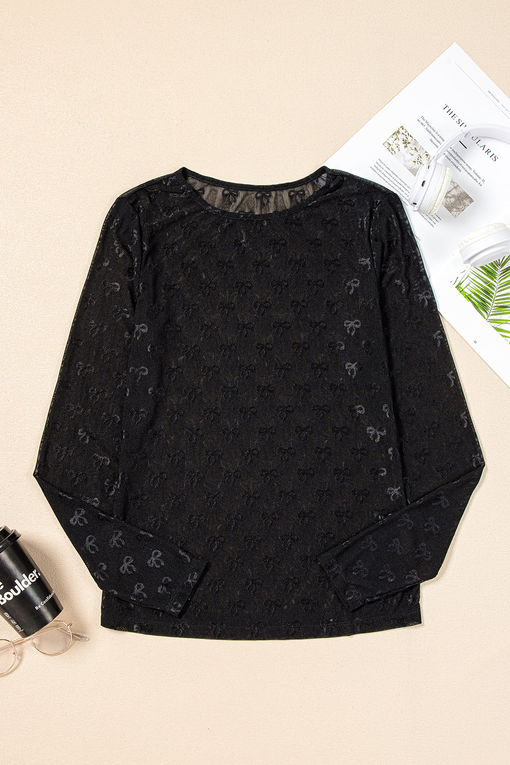 Black long-sleeve top with subtle pattern on a beige surface with a newspaper and cup.