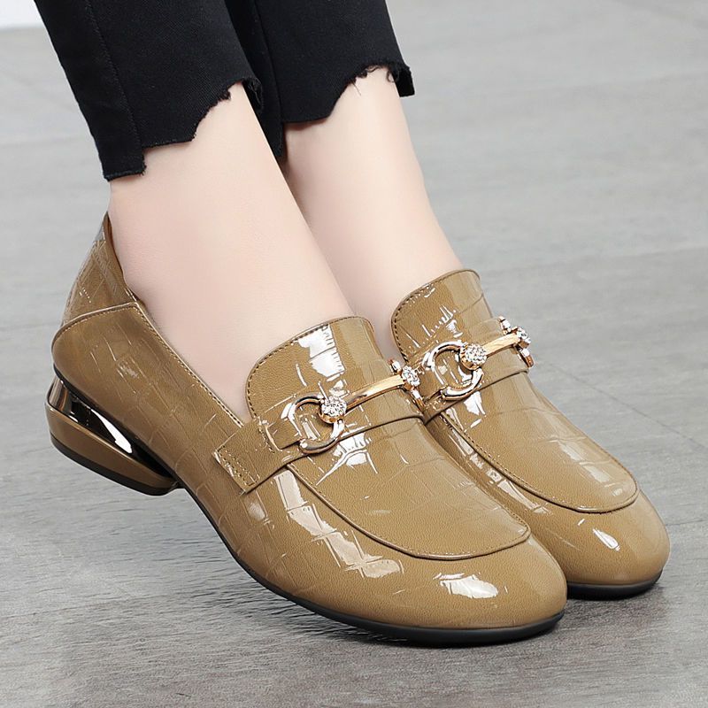 Beige patent leather shoes with a decorative buckle worn by a person on a gray floor.