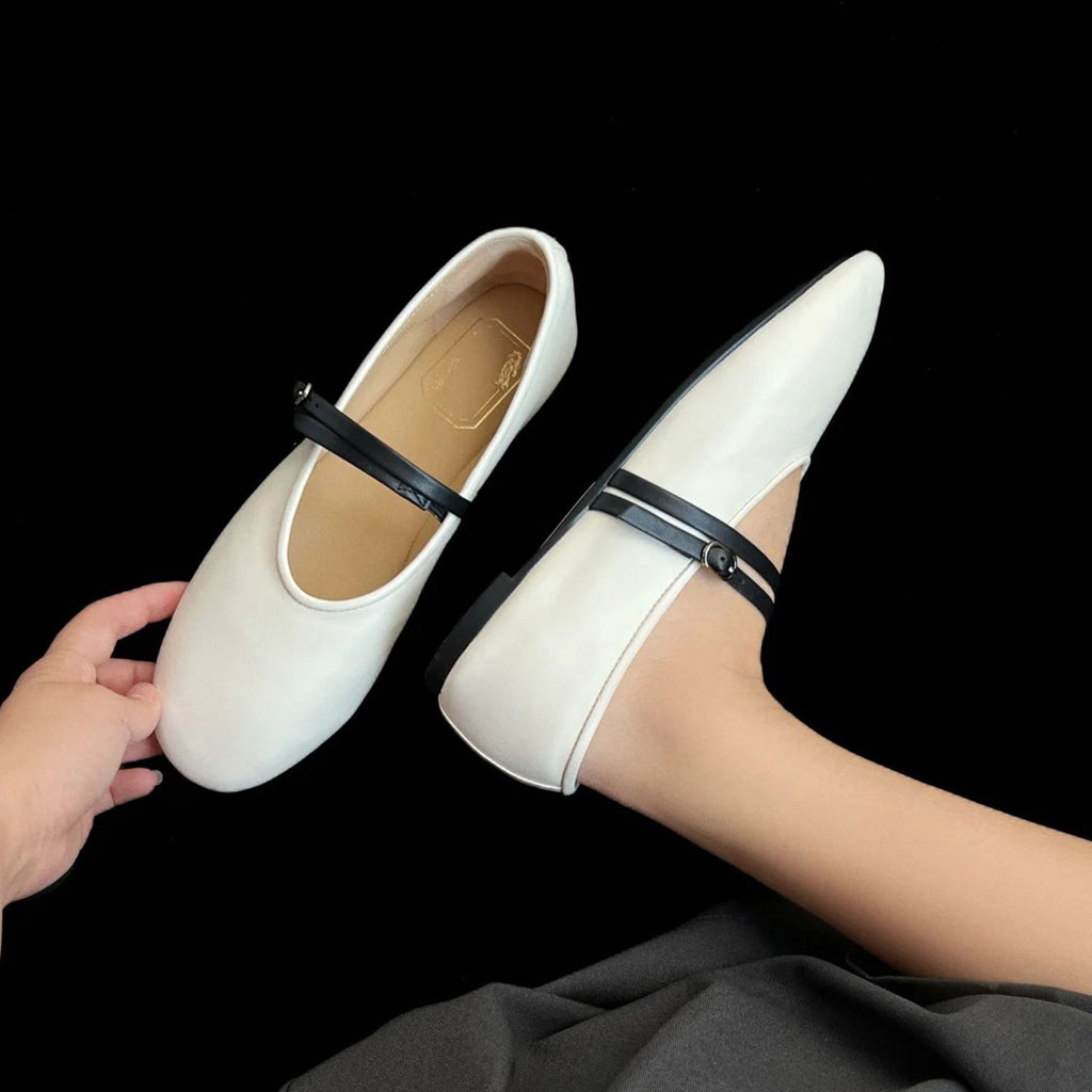 White shoes with black straps held by a hand against a black background