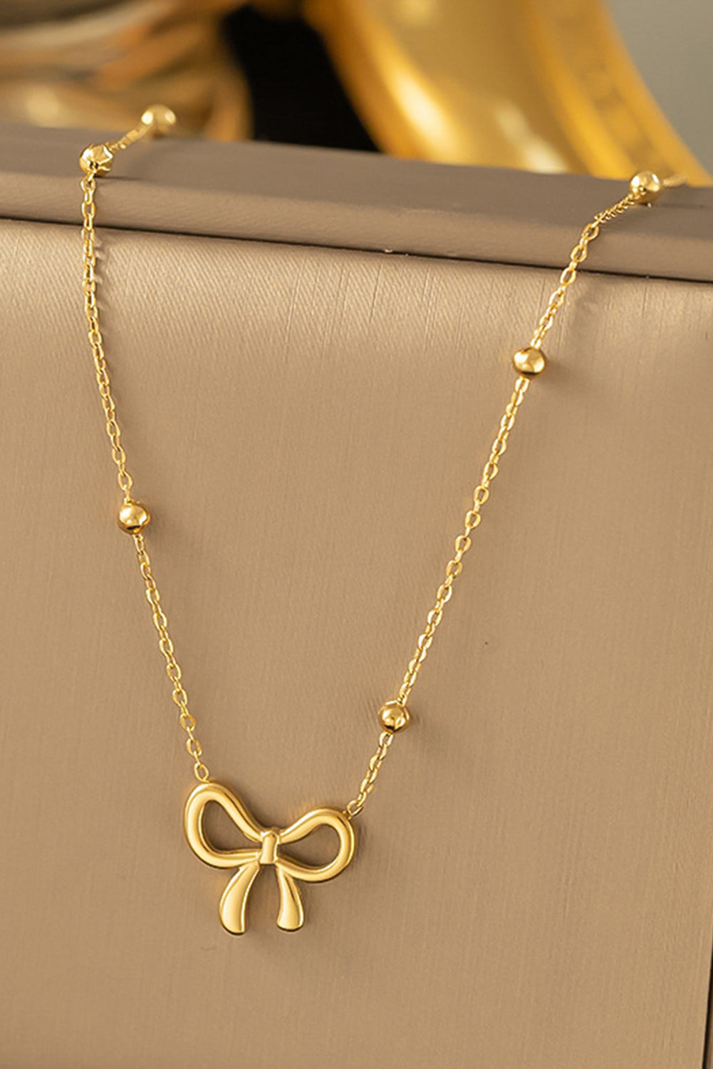 Gold necklace with a bow pendant on a beige surface