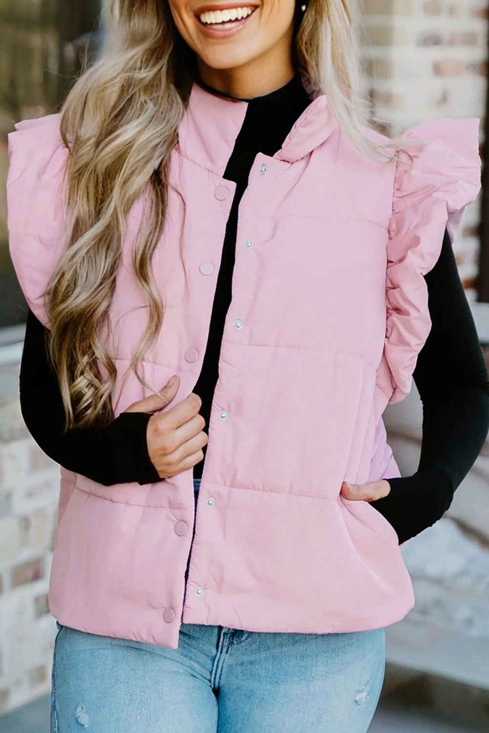 Person wearing a pink puffer vest over a black long-sleeve shirt with a blurred background