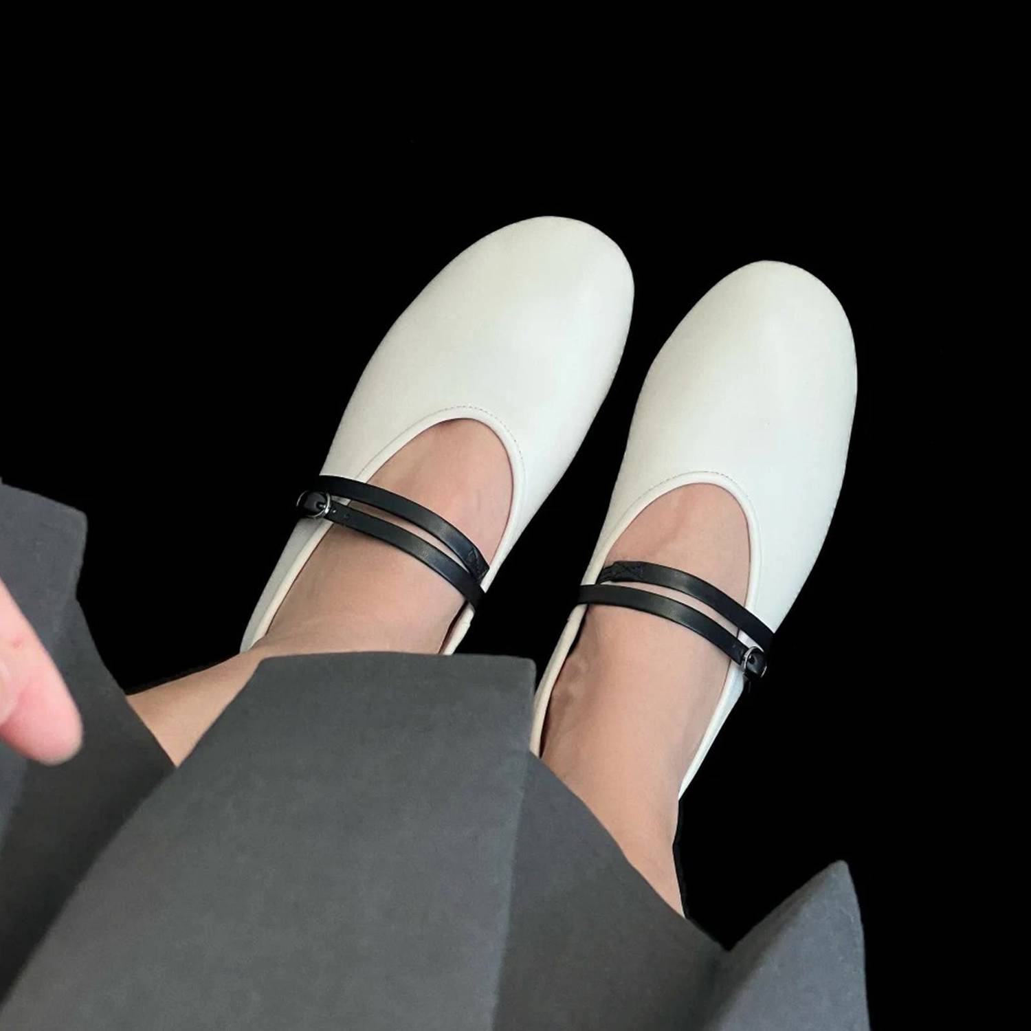 White shoes with black straps worn by a person sitting on a black background