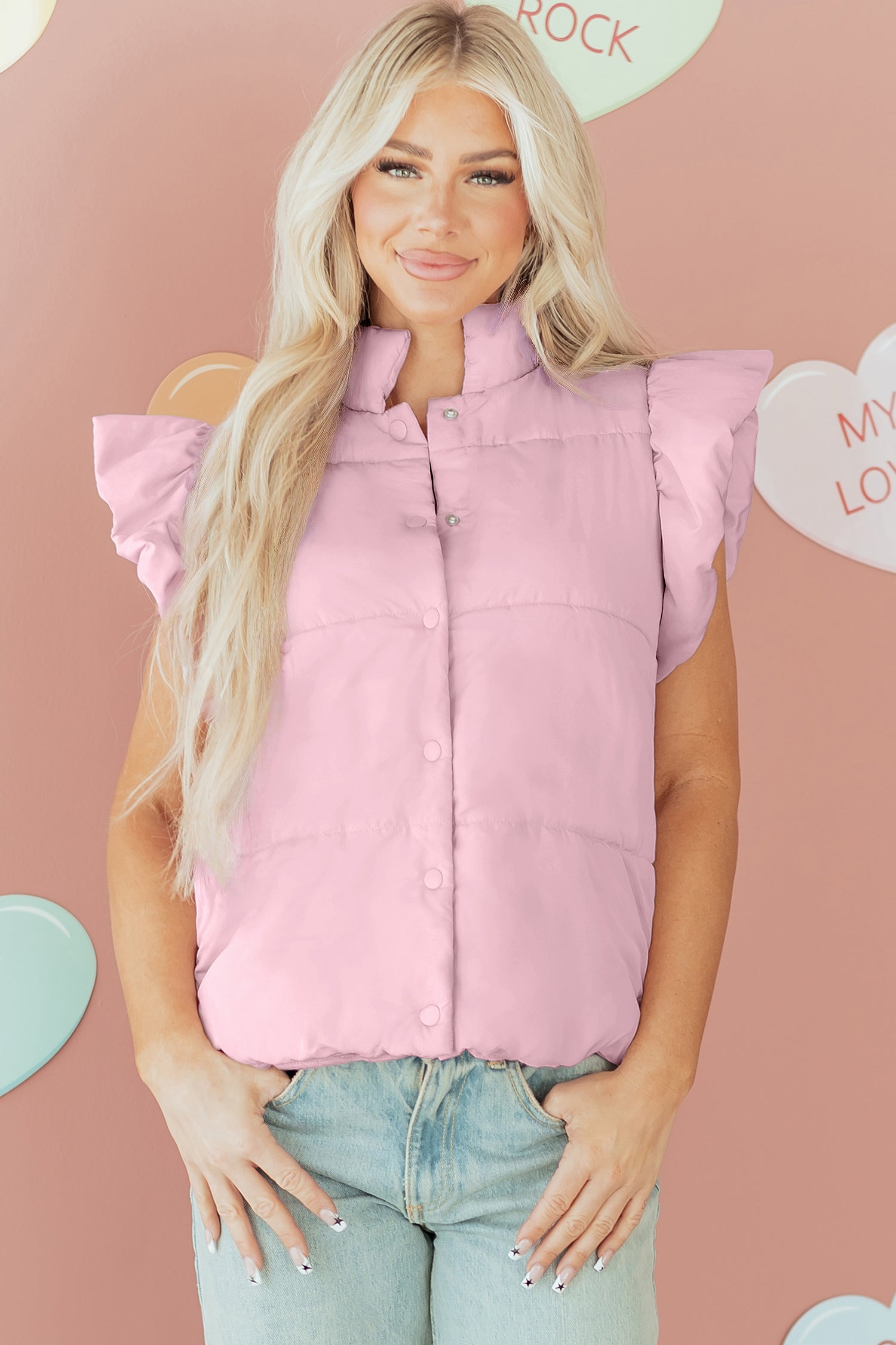 Woman wearing a pink puffer vest against a pink background with heart shapes.