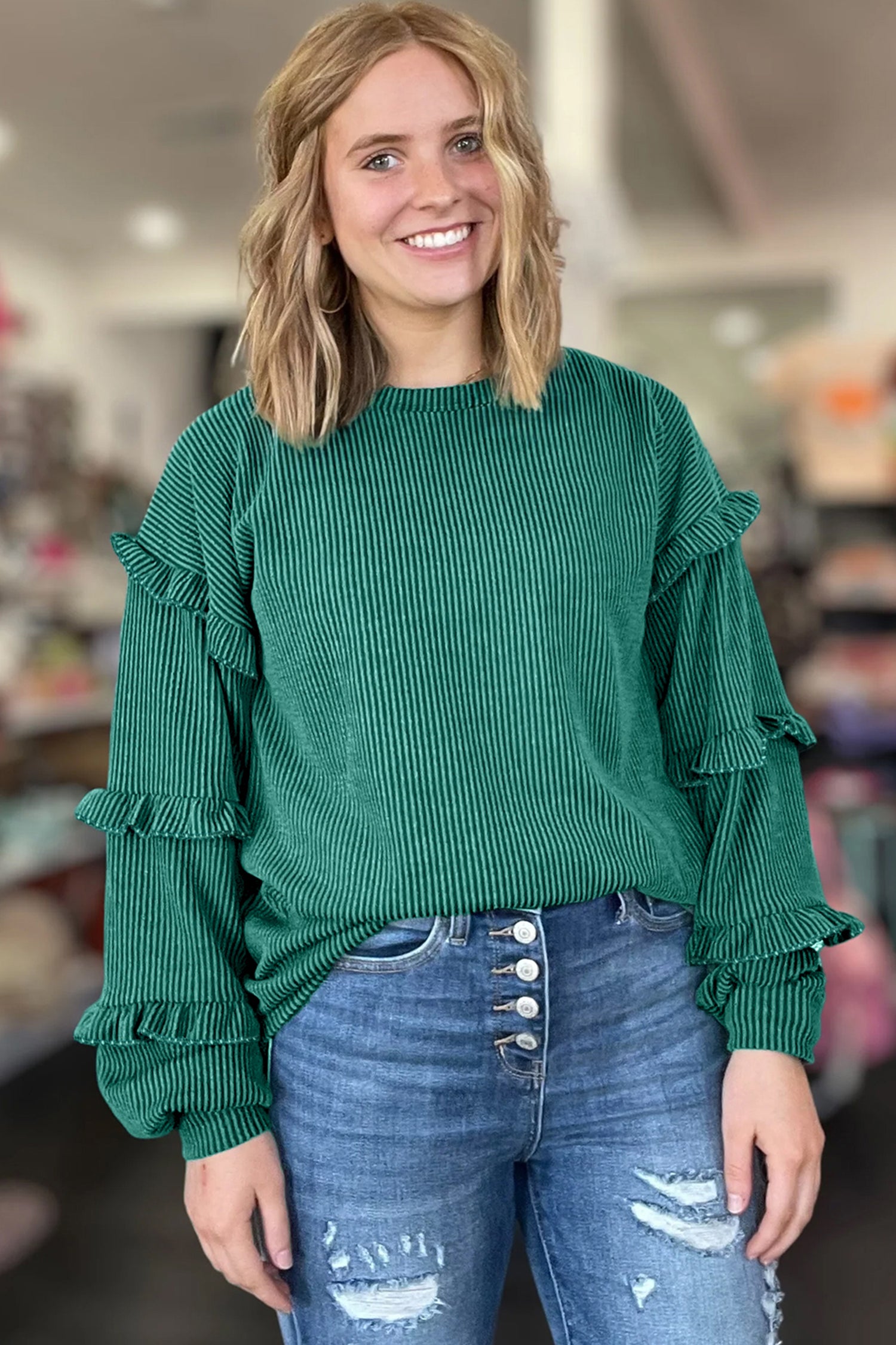 Woman wearing a green ruffled sweater and blue jeans in an indoor setting