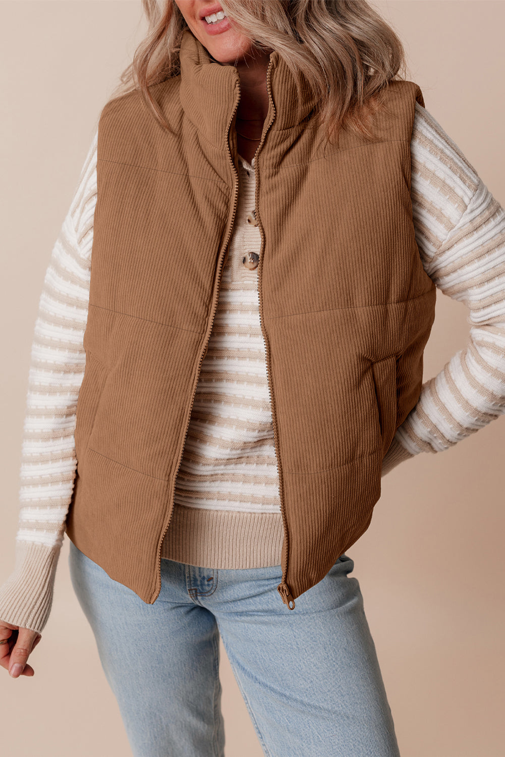 Person wearing a brown corduroy vest over a striped sweater with a beige background