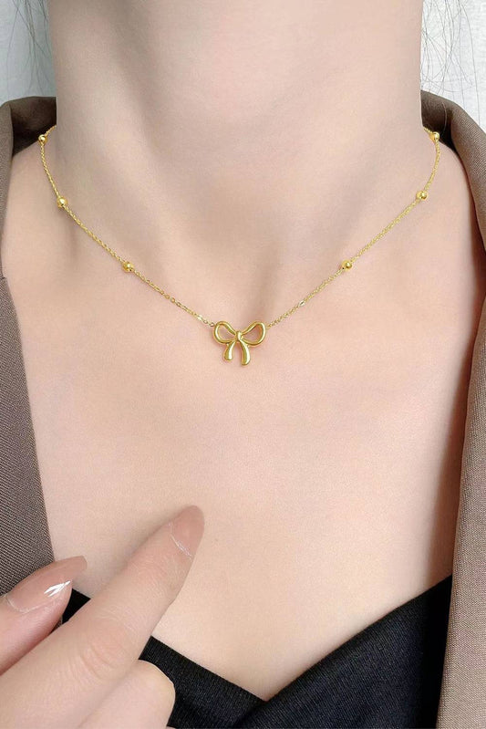 Gold necklace with a bow pendant on a person's neck