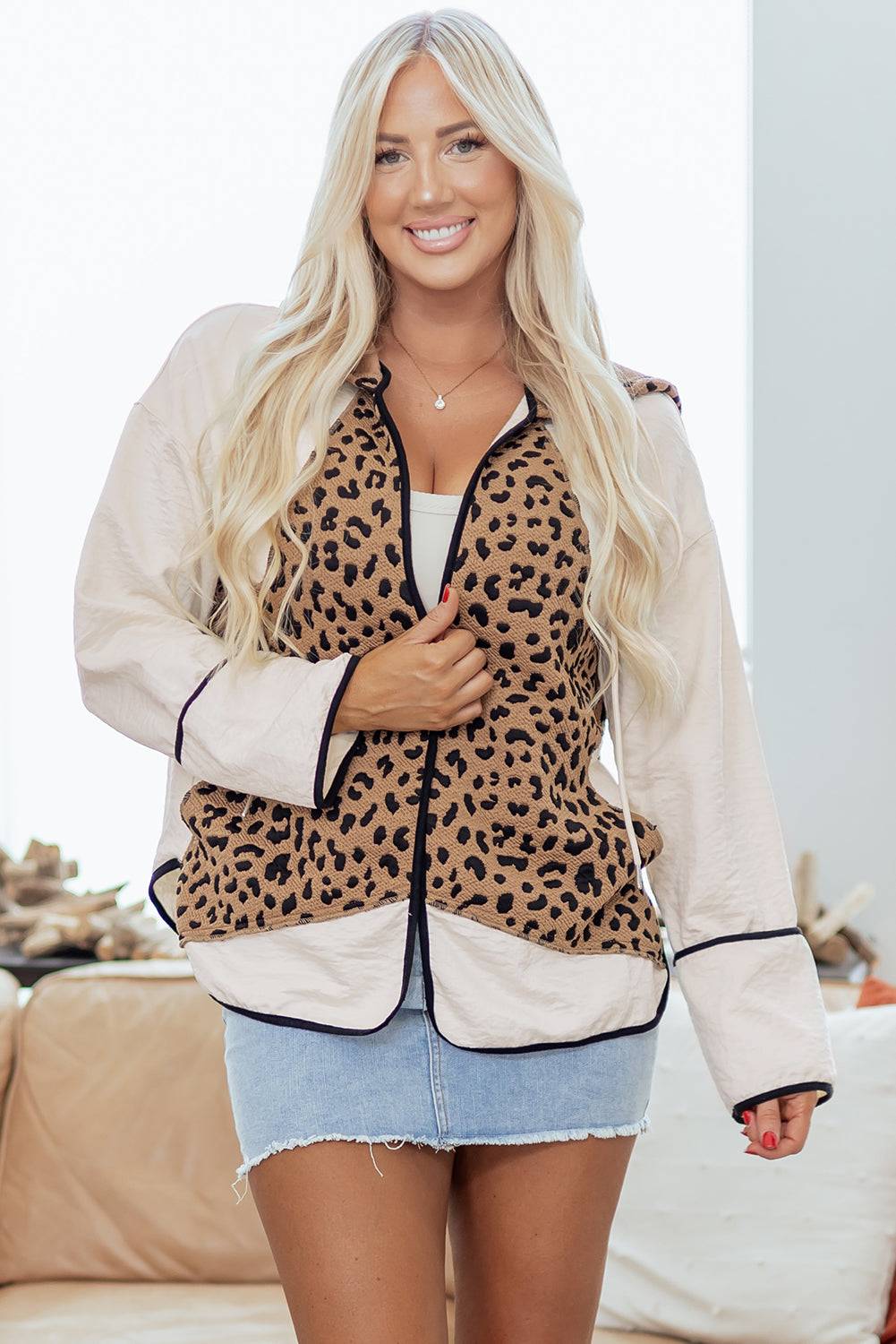 Woman wearing a leopard print jacket over a white top and denim skirt indoors.