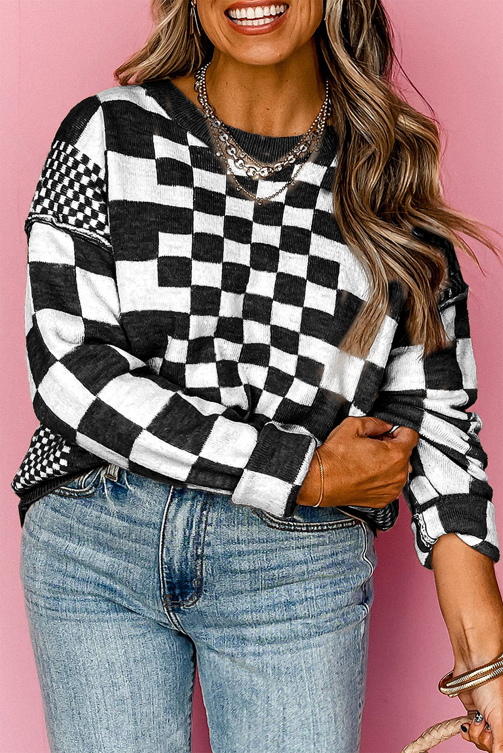Person wearing a black and white checkered sweater with blue jeans against a pink background