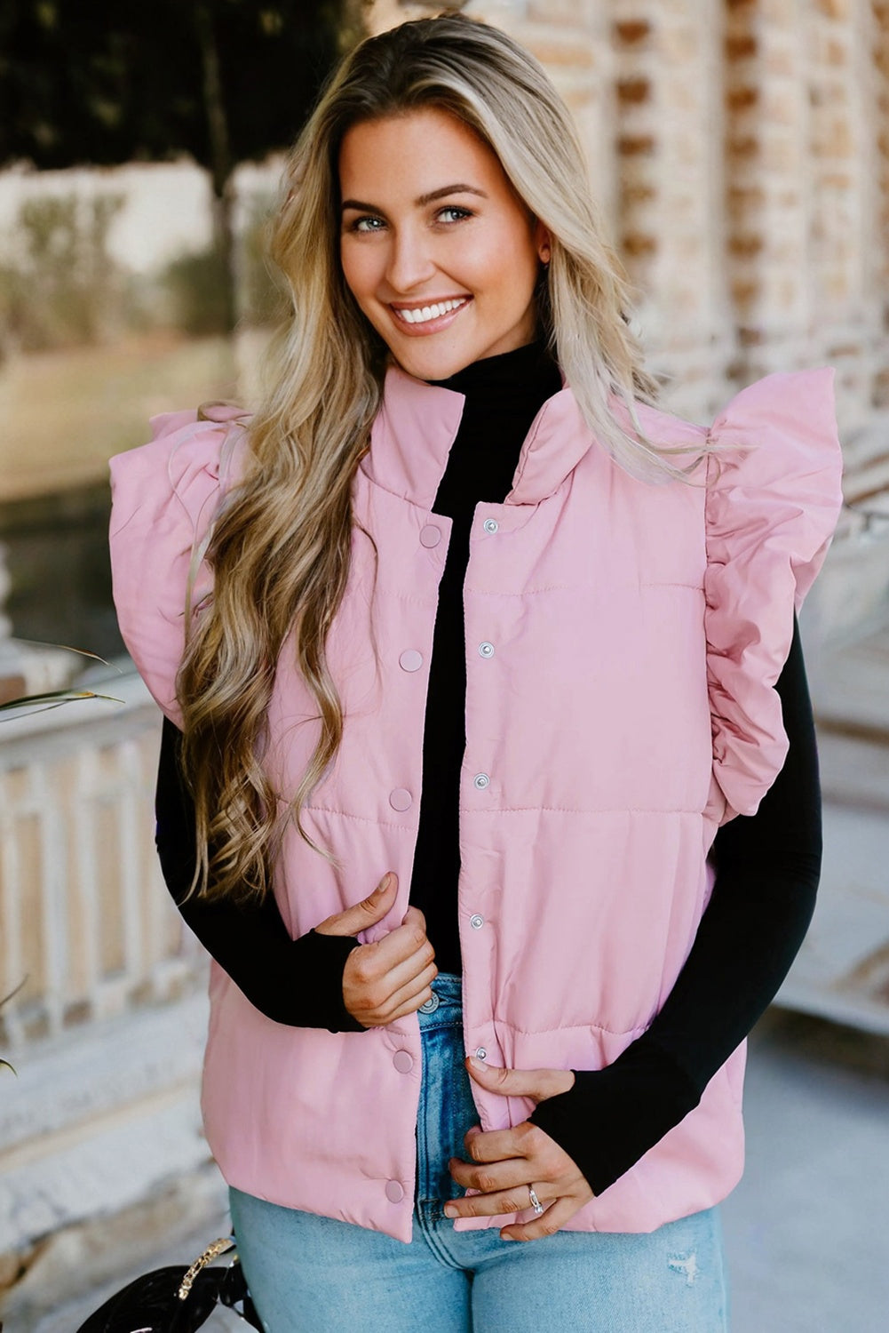 Woman wearing a pink puffer vest over a black long-sleeve shirt, standing outdoors.