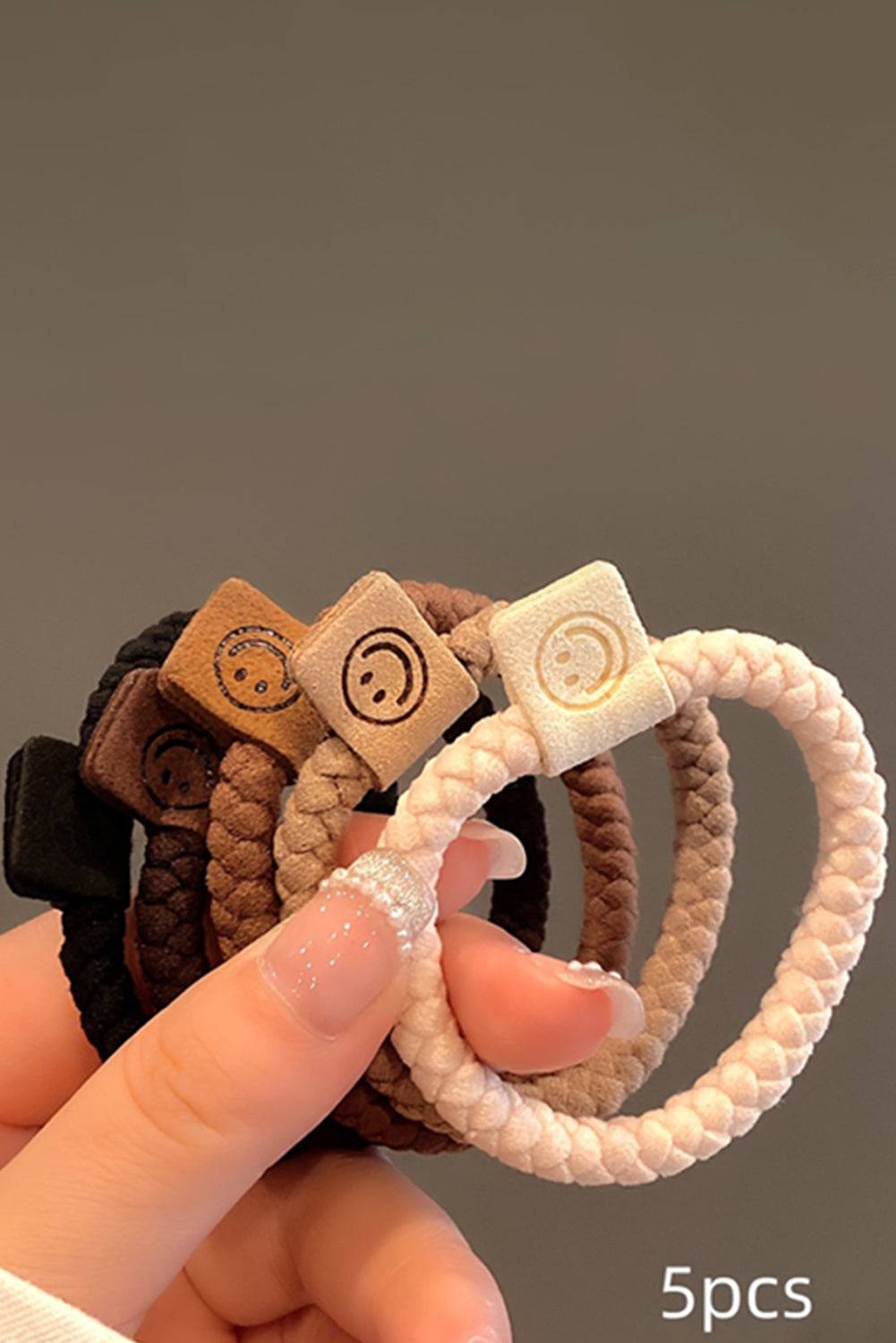 Set of five hair ties with decorative ends held by a hand against a neutral background