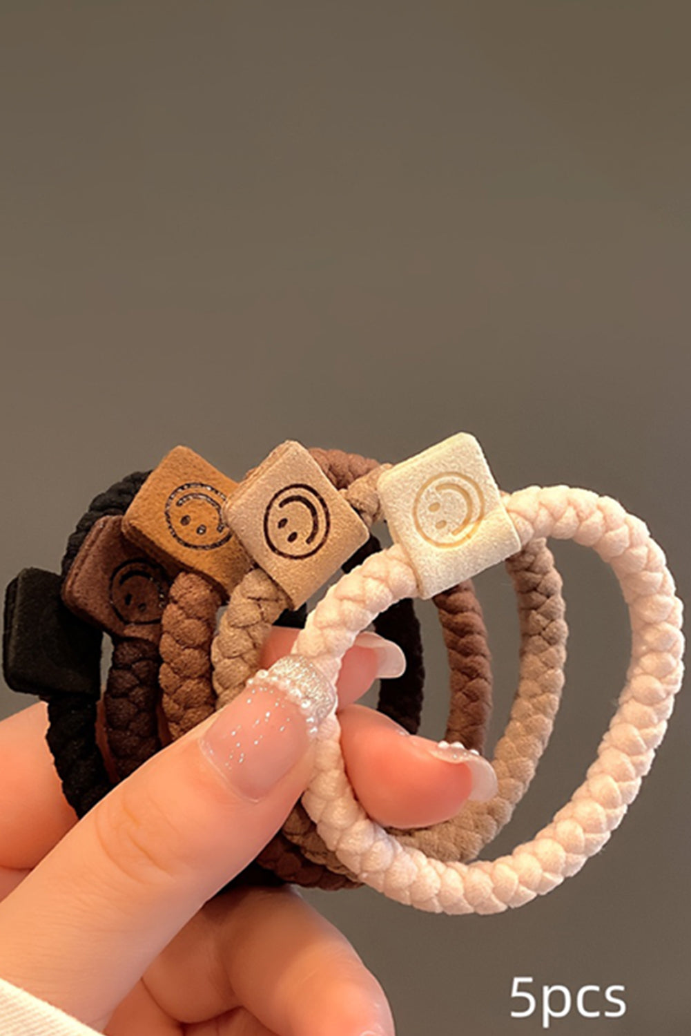 Set of five hair ties with decorative ends held by a hand against a neutral background