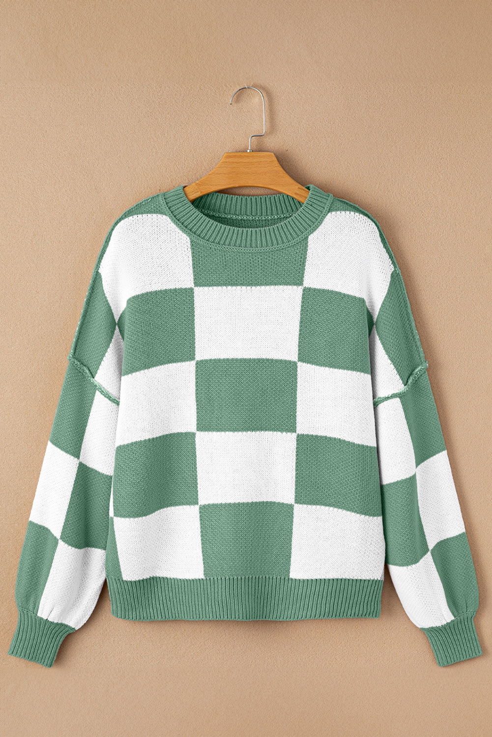 Green and white checkered sweater on a wooden hanger against a beige background