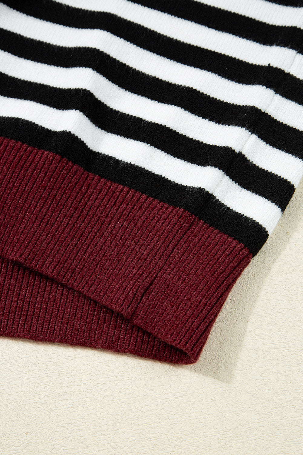Close-up of a sweater with black and white horizontal stripes and a red cuff on a beige background