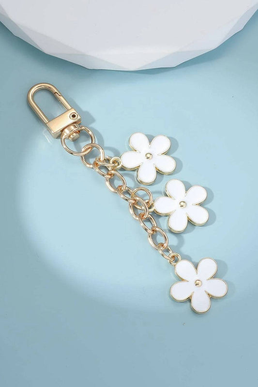 Gold keychain with white flower charms on a light blue background