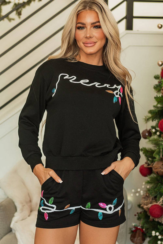 Woman wearing a black outfit with colorful text and light bulb designs, standing in front of a Christmas tree.