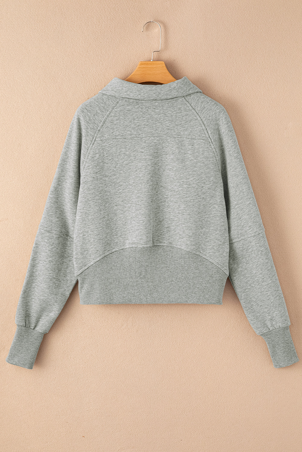 Gray sweatshirt on a wooden hanger against a beige background