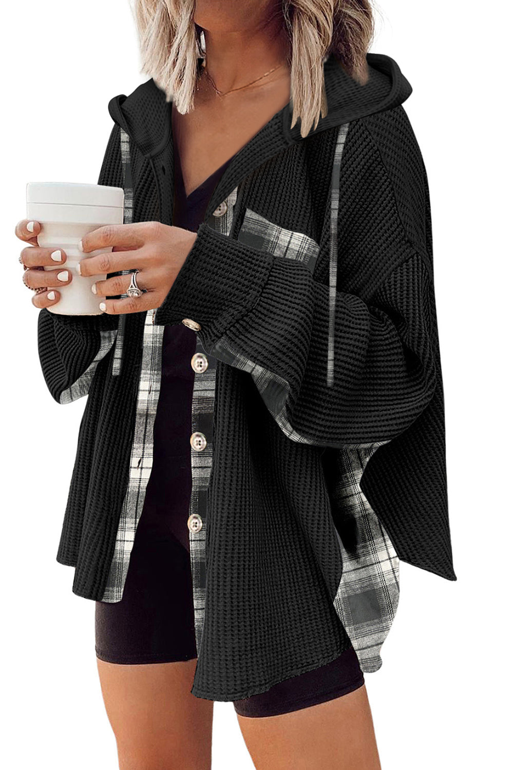 Person wearing a black and plaid cardigan holding a white cup.