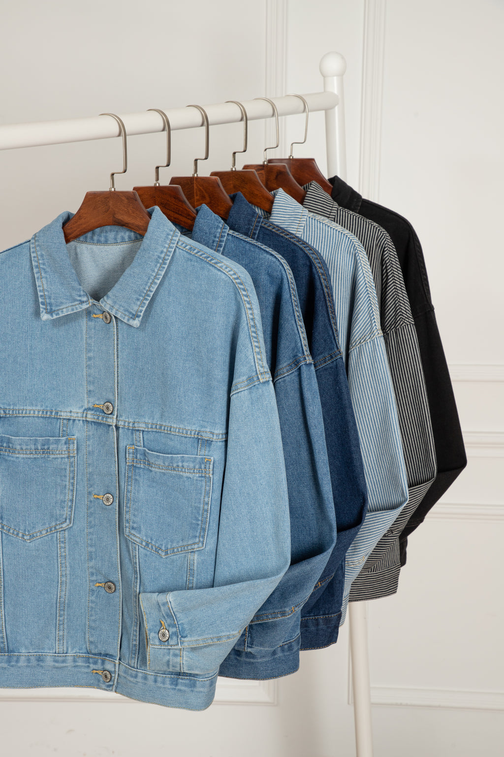 Row of denim jackets on hangers against a white wall