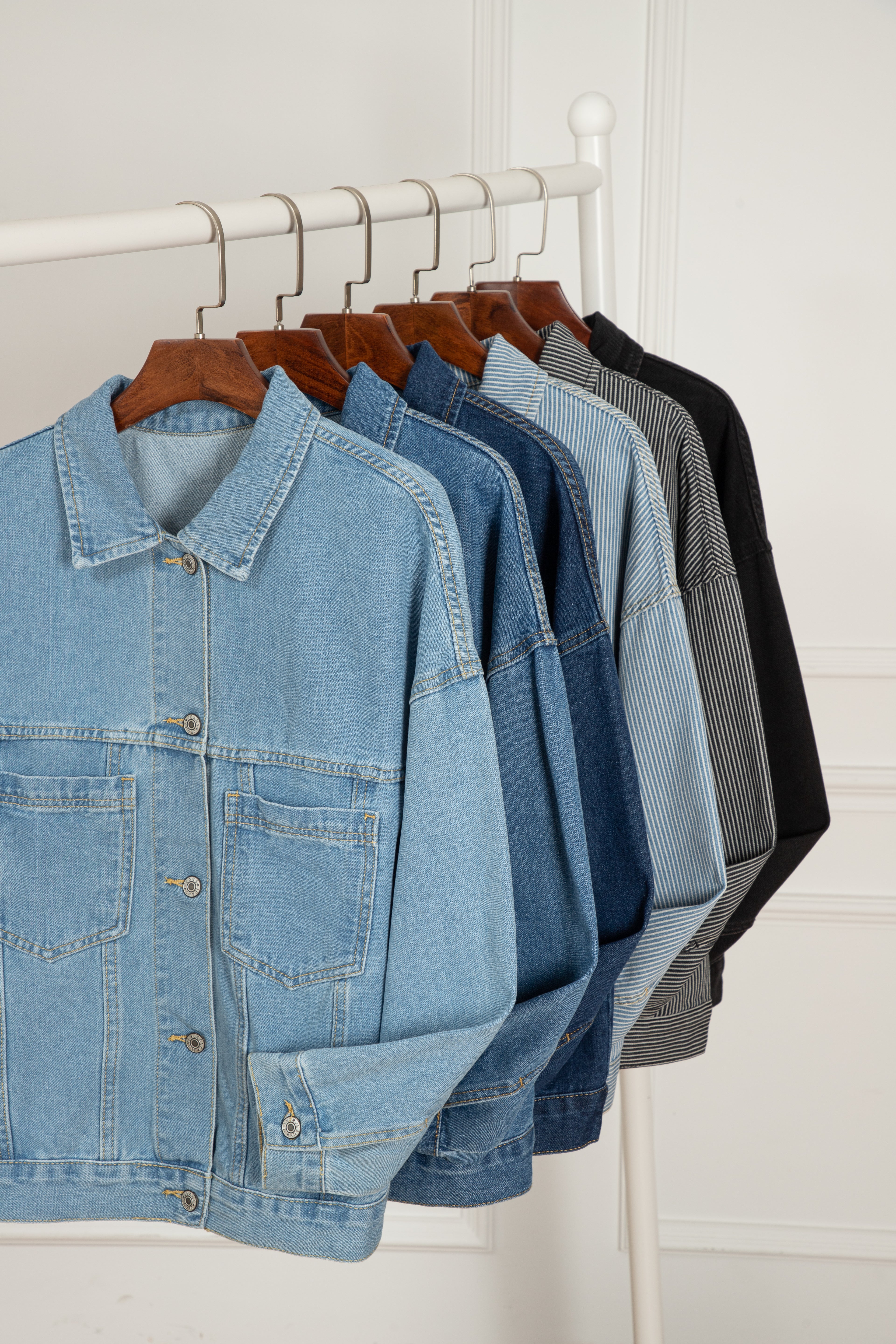 Row of denim jackets on hangers against a white wall