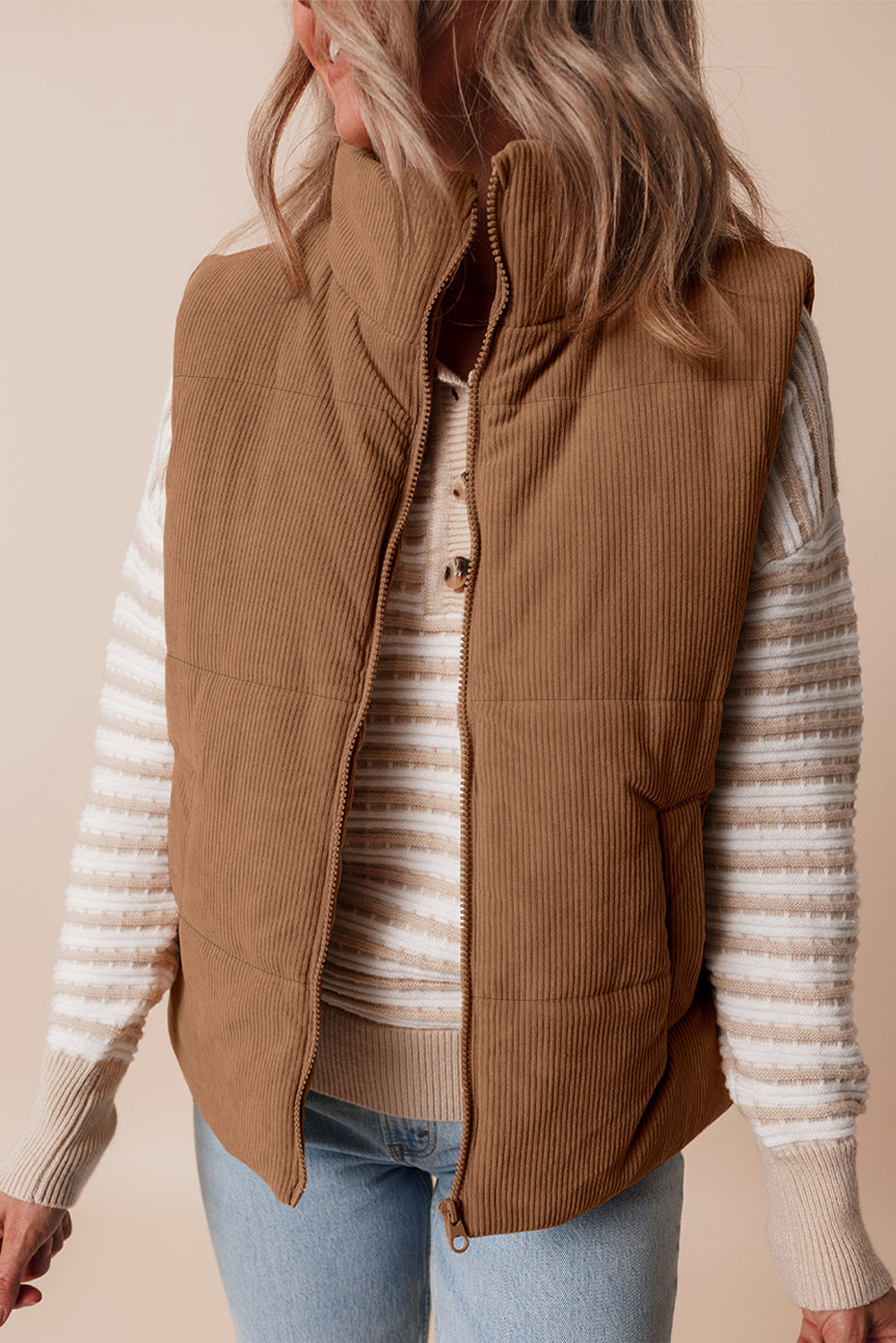 Person wearing a brown vest over a striped sweater with a beige background