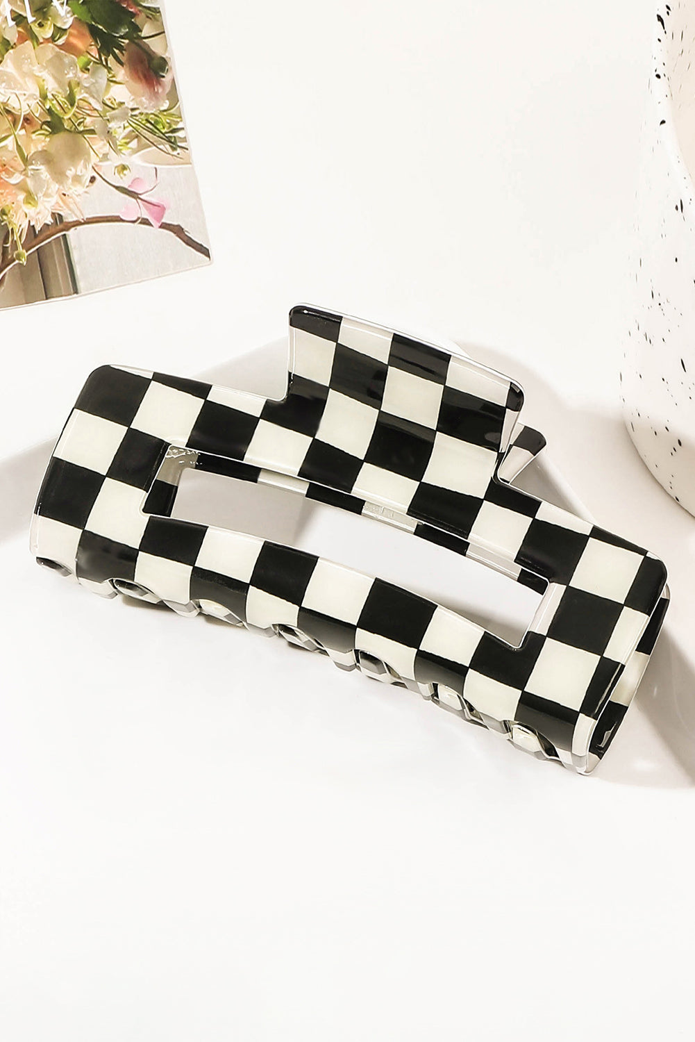 Black and white checkered clutch bag on a light surface with a blurred floral background