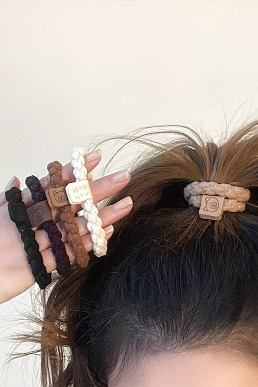 Close-up of a person's hair with multiple hair ties and a hair bun against a neutral background
