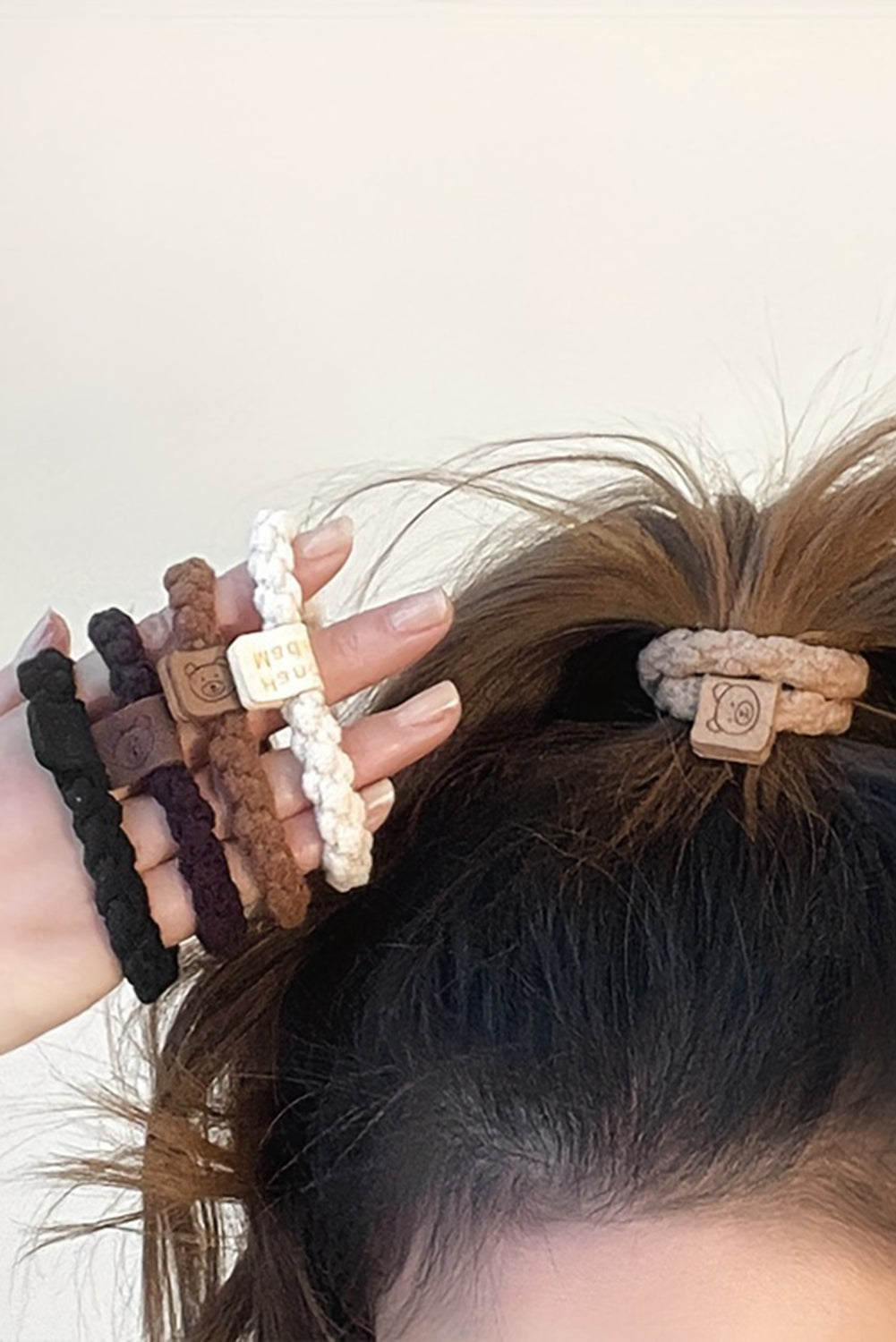 Close-up of a person's hair with multiple hair ties and a hair bun against a neutral background