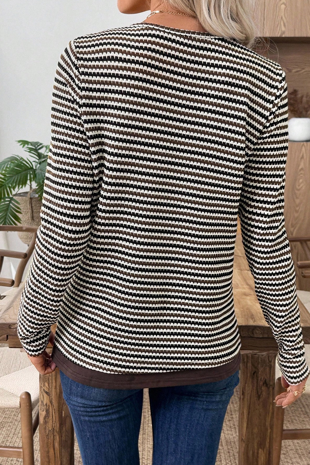 Person wearing a black and white striped sweater with blue jeans indoors.