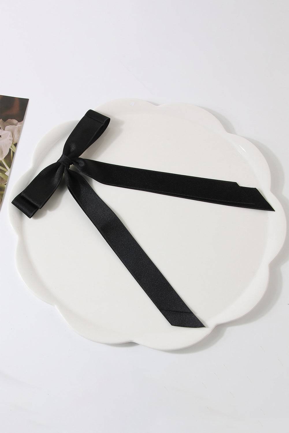 White scalloped-edge plate with a black ribbon on a white background