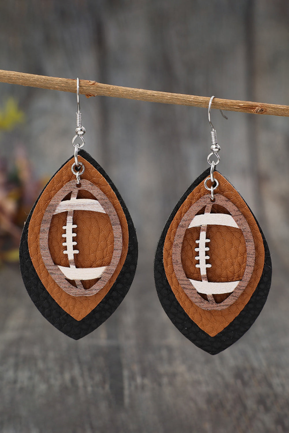 Wooden football-shaped earrings on a branch with a blurred natural background